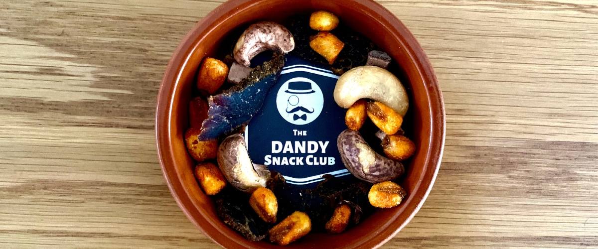 A bowl of nuts from the dandy snack club on a wooden table